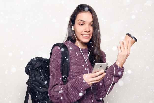 Schnee, Winter, Weihnachten, Technologie, Lifestyle, Internetsucht und Menschenkonzept - Junge schöne Frau mit Smartphone. lächelnde attraktive Frau, die den Handyschneehintergrund betrachtet