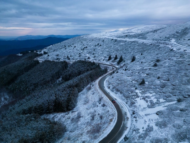 Schneebedeckte Berge bei Sonnenuntergang mit einer kurvenreichen Straße im Vordergrund Luftbild