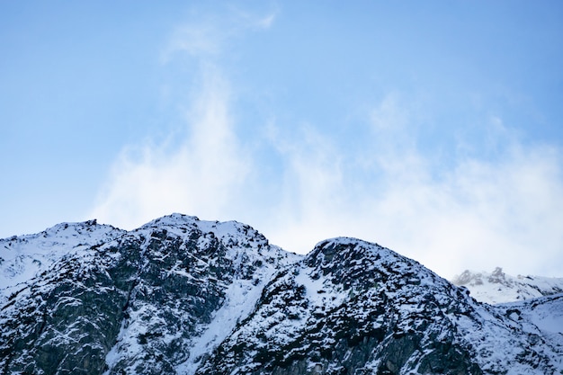 Schneebedeckte Berge in den Alpen. Wolken fliegen in der Nähe der Gipfel der Berge