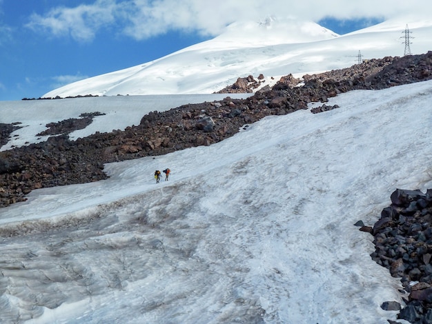 Schneebedeckte Berglandschaft von Elbrus an einem sonnigen Sommertag. Die beiden Reisenden klettern auf einer verschneiten Straße in den Bergen.