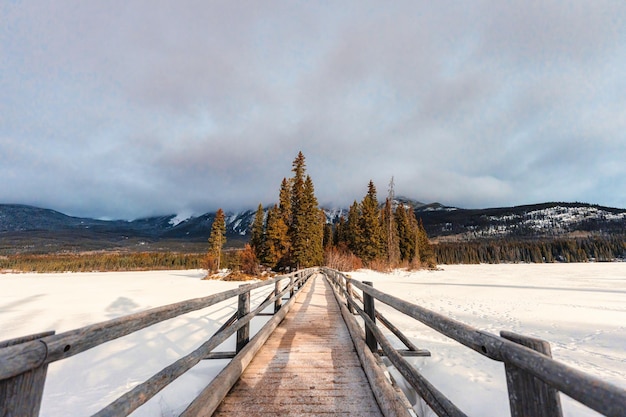 Schneebedeckte Holzbrücke und winziger Kiefernwald am Pyramid Lake im Winter im Jasper-Nationalpark