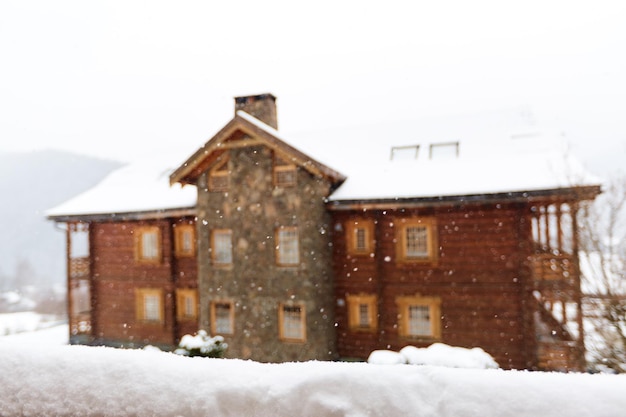 Schneebedeckte Oberfläche für die Produktplatzierung Verschwommenes Haus aus Holz und Stein im Hintergrund Schneefall am Wintertag Weihnachtshintergrund mit Holzhütte oder Chalet im Skigebiet Copyspace