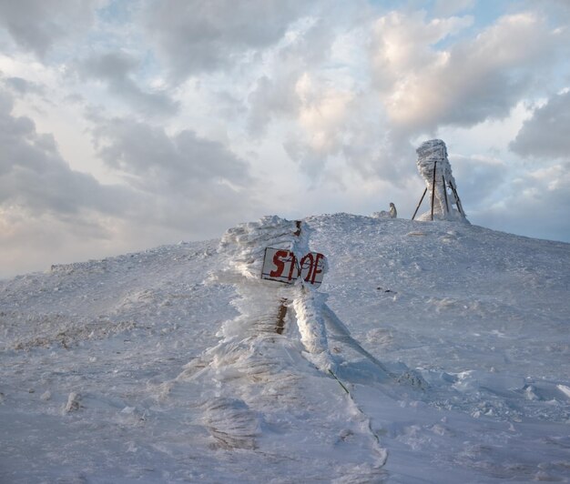 Schneebedeckter Winterbergsobertag im letzten Abend Sonnenlicht vor Schneesturm Windfrost auf Zeigen und Stoppschildern über gefährlichen Abgrund