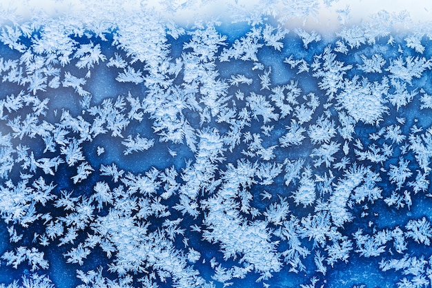 Schneeflocken und blauer Frost auf Glas im Winter