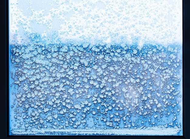 Schneeflocken und Frostmuster auf gefrorenem Fenster