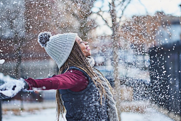 Schneeflocken wie Küsse vom Himmel Aufnahme einer glücklichen jungen Frau, die an einem Wintertag im Freien Schnee wirft