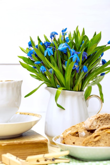 Schneeglöckchen in einer Vase, eine Tasse Tee und Biscotti auf dem Tisch