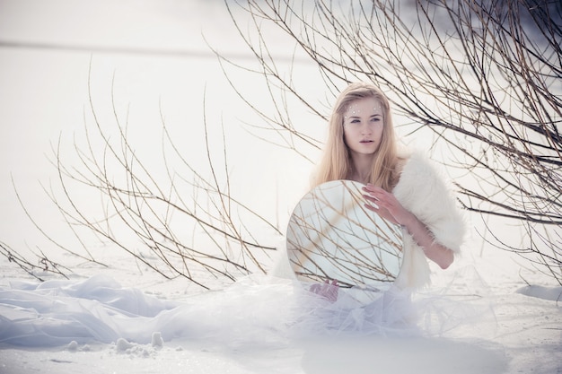 Schneekönigin. Ein junges Mädchen im Bild der Eisprinzessin im Schnee auf einer Winterlandschaft. Geheimnisvolles sinnliches Bild einer Frau an einem kalten Wintermorgen