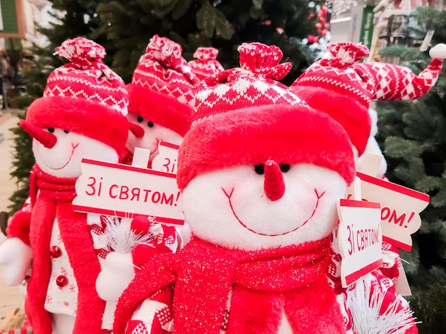 Schneemänner werden an den Theken in der Nähe der Weihnachtsbäume im Einkaufszentrum verkauft, gekleidet in eine rote Mütze und mit einem Schild mit Aufschriften