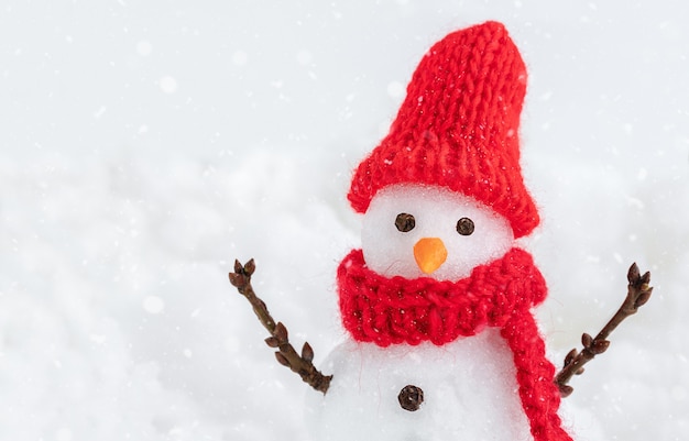 Schneemann in roter Mütze und Schal auf dem Schneehintergrund