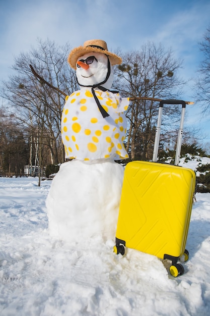 Schneemann mit Koffer bereit für die Reise in den tropischen Landkopierraum