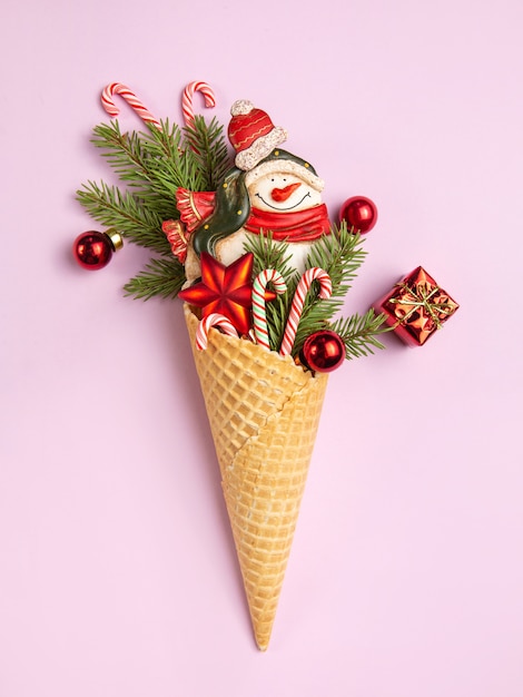 Foto schneemann, weihnachtsbaumzweige und lutscher in einem waffelkegel. ein originelles süßes geschenk. rosa wand.