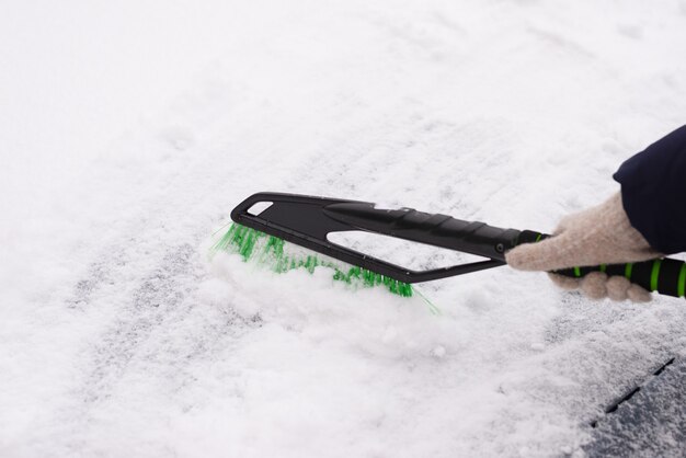 Schneeräumung, Auto im Schnee. Frau reinigt das Auto vom Schnee.