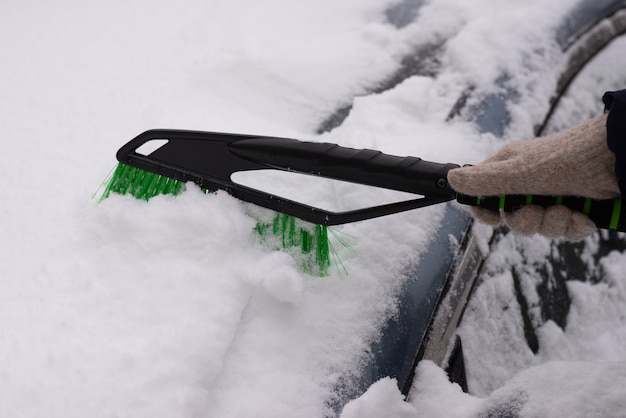 Schneeräumung, Auto im Schnee. Frau reinigt das Auto vom Schnee.