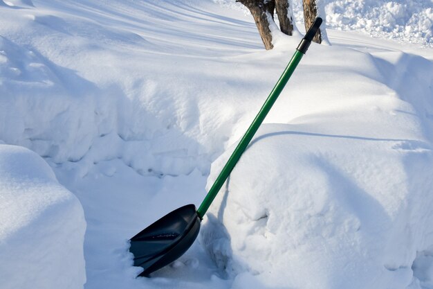 Schneeräumung. Schneeschaufel, umgeben von großen Schneeverwehungen. Hilfsmittel für die winterliche Straßenreinigung.