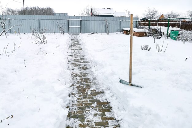 Schneeschaufel mit Holzgriff - Wegbereiter in Schneeverwehung auf Landgrundstück. Winterarbeiten für die Pflege des Landhauses. Schneeräumarbeiten