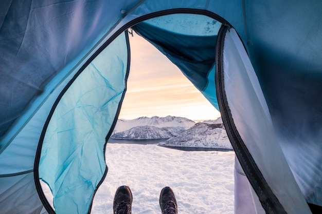 Schneeschuhe, die sich im Zeltcampingeingang mit Landschaftsschneekamm bei Sonnenaufgang entspannen