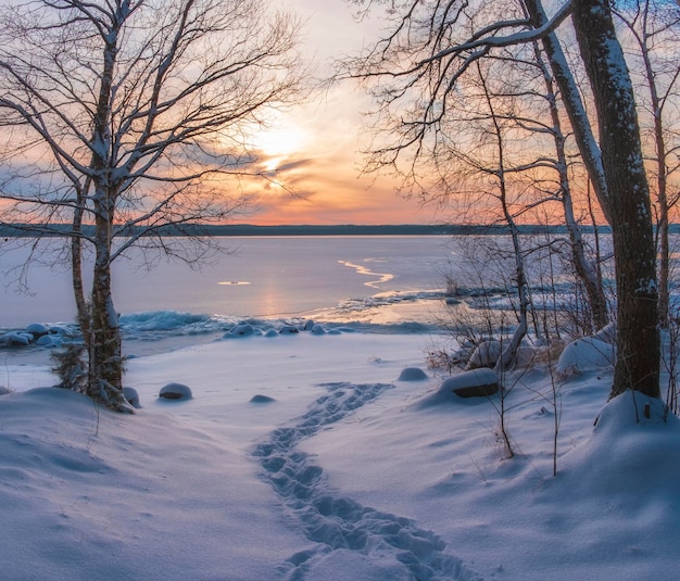 Schneeweg zum See unter Eis bei Sonnenuntergang. Winterlandschaft.