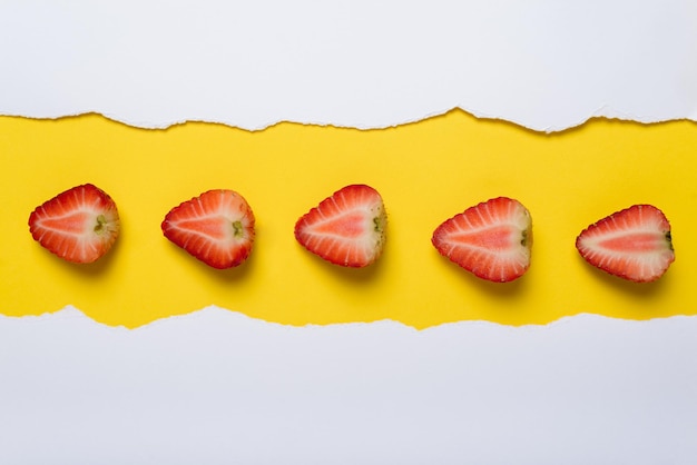 Schneide Erdbeeren auf gelbem Hintergrund mit zerrissenen weißen Papierkanten Close-up Sommer-Hintergrund