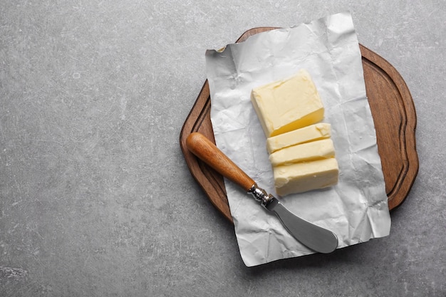 Schneidebrett mit Stück unverpackter geschnittener Butter und Messer auf grauem Hintergrund