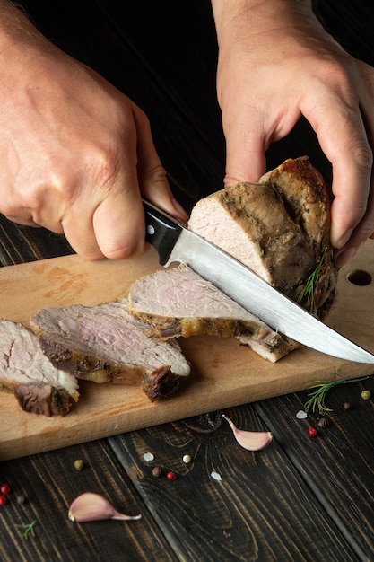 Schneiden eines saftigen Rindersteaks mit einem Messer in den Händen eines Küchenchefs Nahaufnahme Das Konzept des Kochens Dunkler Hintergrund für Werbung oder Rezept
