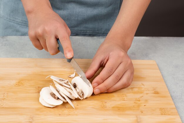 Schneiden Sie Champignonpilze auf einem Holzbrett, bereiten Sie Salat, gesundes Essen mit Gemüse und Ernährung vor