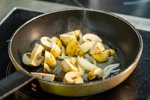 Schneiden Sie Champignons mit Zwiebeln auf einer brutzelnden Bratpfanne. Rauchen Sie dünn über der heißen Bratpfanne aus der Nähe