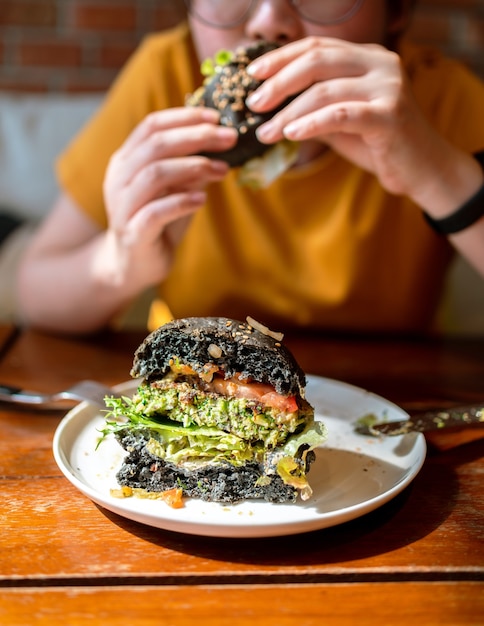 Schneiden Sie die Hälfte des Broccoli-Quinoa-Holzkohle-Burgers mit Guacamole, Mango-Salsa und frischem Salat, serviert auf einem weißen Teller. Kreatives veganes Essen für Vegetarier.