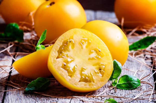 Schneiden Sie große gelbe Tomaten und grüne Blätter des selektiven Fokus des hölzernen Hintergrundes der Basilikumweinlese