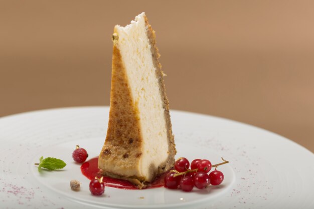 Schneiden Sie Käsekuchen mit Waldfrüchten und roten Johannisbeeren, Minze und Goldblatt auf weißer Platte