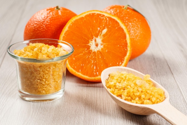 Schneiden Sie Orange mit zwei ganzen Orangen, Glasschüssel und Holzlöffel mit gelbem Meersalz auf Holztisch. Spa-Produkte und Zubehör. Selektiver Fokus auf eine Schüssel