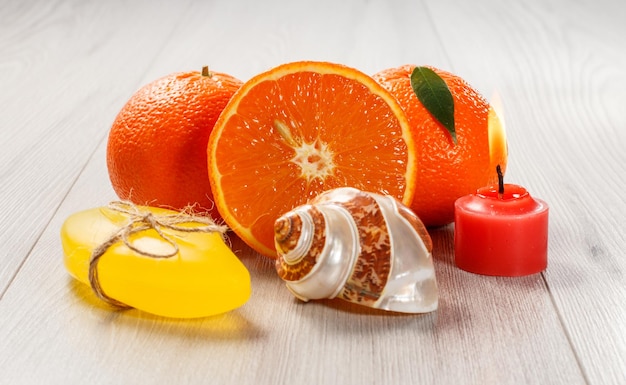 Schneiden Sie Orange mit zwei ganzen Orangen, Seifenmuschel und brennender roter Kerze auf Holzschreibtisch Spa-Produkte