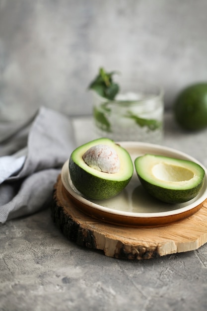 Schneiden Sie reife Avocado auf einem Teller auf einem Holzbrett neben einer Serviette auf einem Grau.