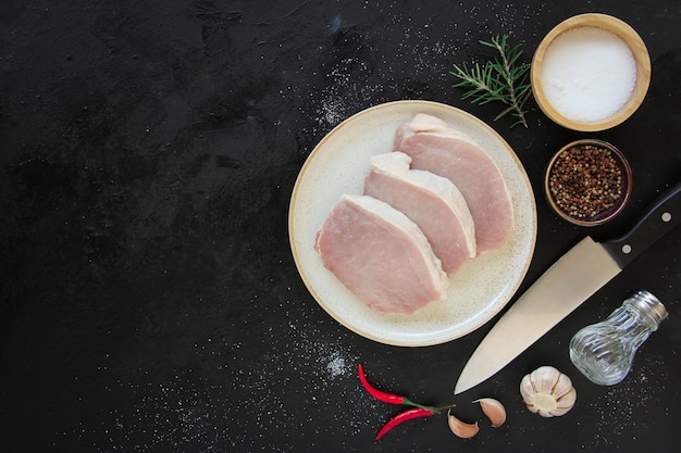 Schneiden Sie rohes Rindfleisch mit Gewürzen in Teller und Rosmarin. Auf dunklem rustikalem Hintergrund. Draufsicht mit Kopierraum.