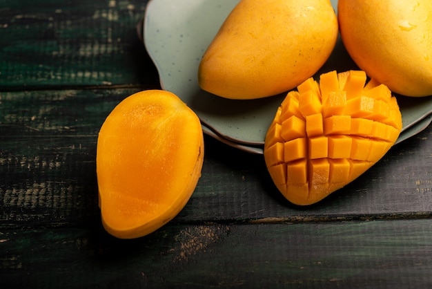 Schneiden und vervollständigen Sie die Mangos auf einem Teller in einer dunklen Umgebung