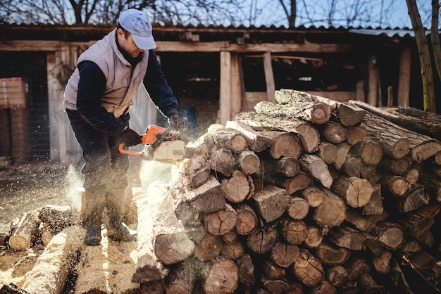 Schneiden von Holz mit Kettensäge im Hinterhof, Holzfällerberuf.