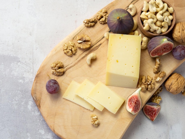 Schneiden von Käse mit Früchten - Nüssen und Feigen auf einem Holzbrett. Leckerer Snack