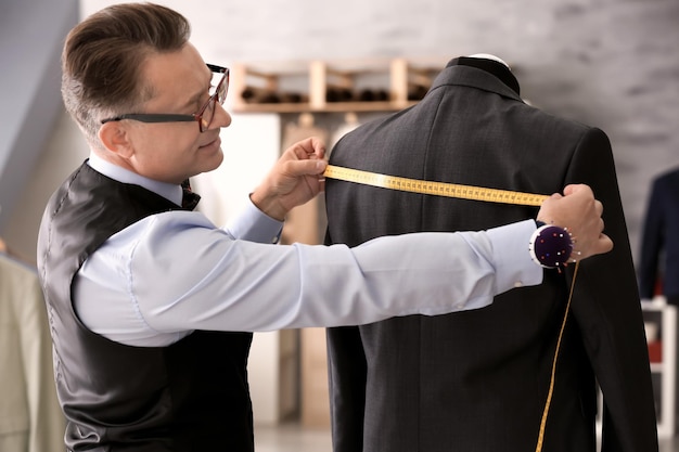 Foto schneider, der im atelier die jacke an der schaufensterpuppe misst