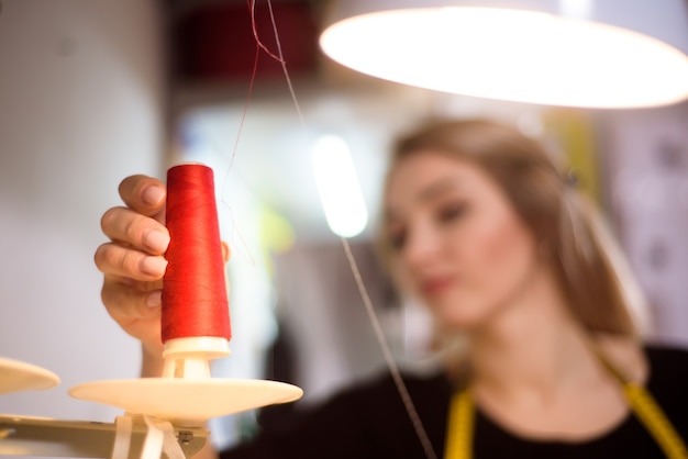 Schneiderarbeit am Arbeitsplatz im Atelier. Nähmaschine, Lineal, Schere, Tischlampe, Fäden im Hintergrund.