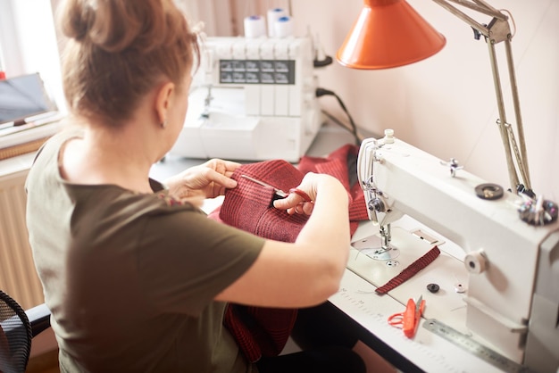 Schneiderin, die im Atelier am Arbeitsplatz sitzt und eine Schere zum Abschneiden des Stoffstücks im Nähprozess verwendet Rückansicht