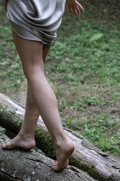 Foto schneidung der beine von frauen, die barfuß auf einem baumstamm im wald laufen