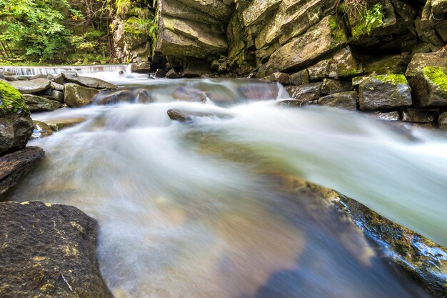 Schnell fließender Flussstrom mit glattem Wasser, das von großen Steinen fällt