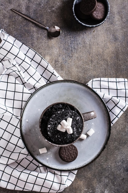 Schneller Schokoladenkuchenbecher mit Marshmallows auf einem Teller auf der Tischplatte und vertikale Ansicht