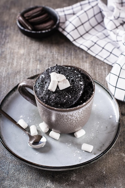 Schneller Schokoladenkuchenbecher mit Marshmallows auf einem Teller auf der vertikalen Tischansicht