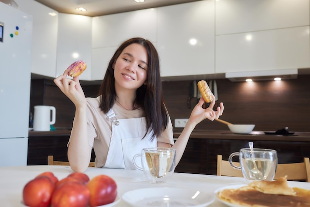 Schnittaufnahme einer Mutter in Rot und ihrer Tochter mit bunten Donuts, die in der Küche sitzen Diätkonzept und Junk Food