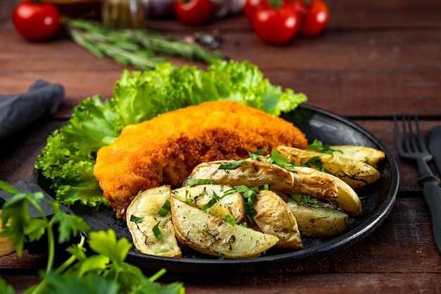 Schnitzel de cerdo con patatas al horno en una sartén sobre una mesa de madera