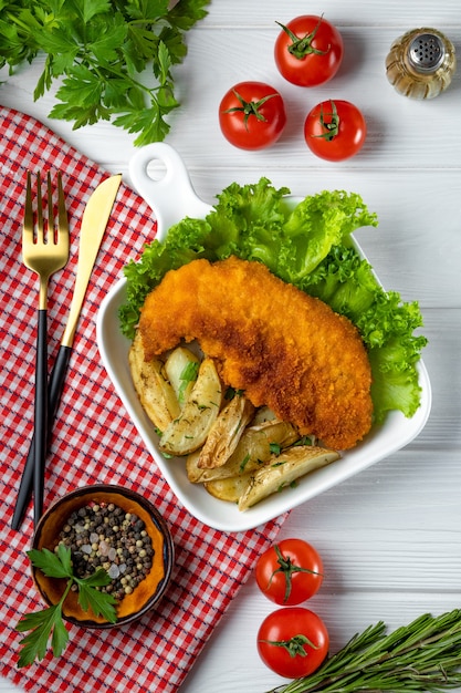 Schnitzel de cerdo con patatas asadas en una madera blanca