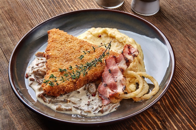 Schnitzel de frango com purê de batata de ervas e molho de cogumelos no prato no fundo da mesa de madeira.