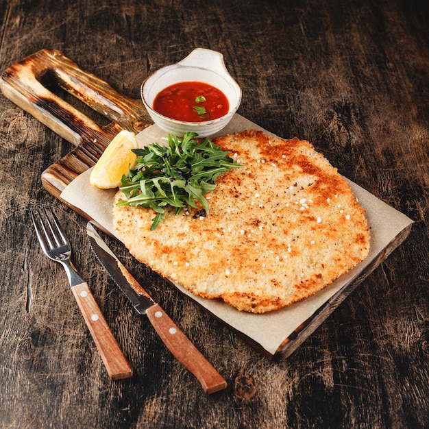 Schnitzel de porco com molho de tomate em fundo escuro de madeira