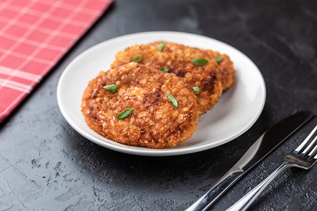 Schnitzel liegen auf einem weißen teller. hühnchenkoteletts liegen zwischen dem gemüse auf einem schwarzen steintisch.